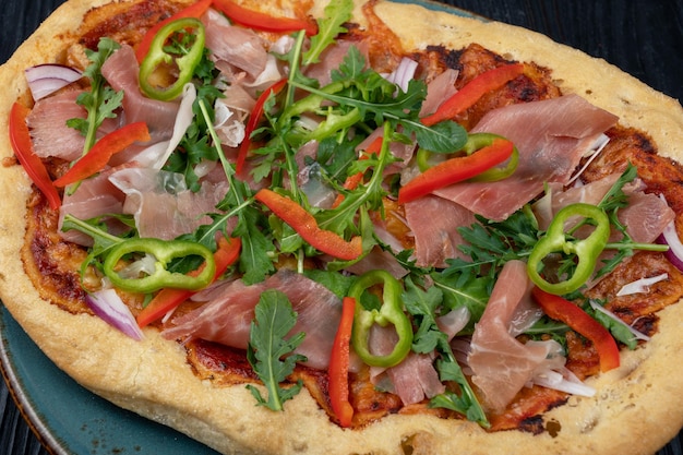 Italienische Pizza auf Teller mit Jamon-Scheiben Pfeffer und frischen Rucola-Blättern an der Spitze