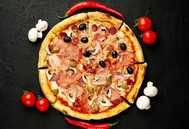 Italienische Pizza mit Speck, Pilzen, Oliven, Tomaten auf einem schwarzen Betonhintergrund