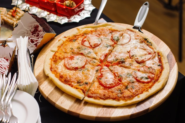 Italienische Pizza mit Tomate, belegt mit geschmolzenen Käsekräutern und Basilikum, serviert auf einem runden Holzbrett