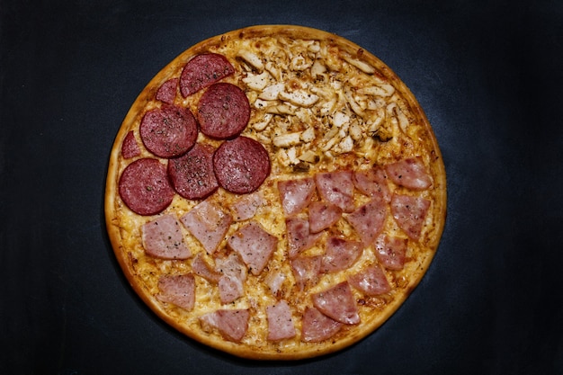 Italienische Pizza mit vier Fleischsorten auf hölzernem schwarzem Hintergrund Draufsicht lecker und appetitlich
