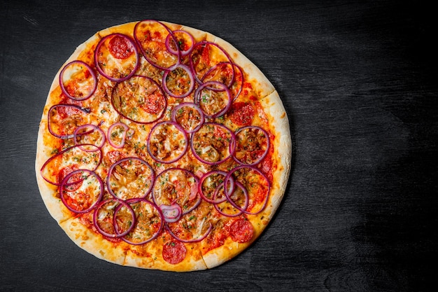 Italienische Pizza mit Wurst- und Zwiebelringen auf schwarzem Hintergrund, Draufsicht. Hochwertiges Foto