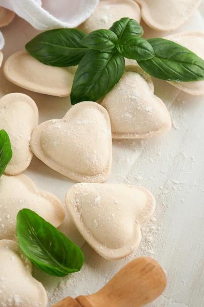 Italienische Ravioli-Nudeln in Herzform. Leckere rohe Ravioli mit Mehl und Basilikum auf weißem Hintergrund. Hintergrund für Lebensmittelzutaten. Ideen für das Mittagessen zum Valentinstag oder Muttertag. Draufsicht mit Kopierraum