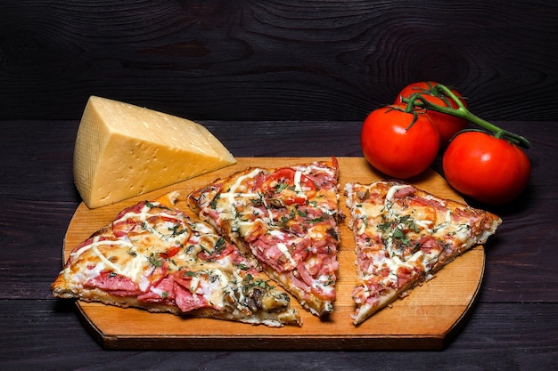 Italienische rustikale Pizza drei Stücke auf einem dunklen Holztisch mit Tomaten und Käse