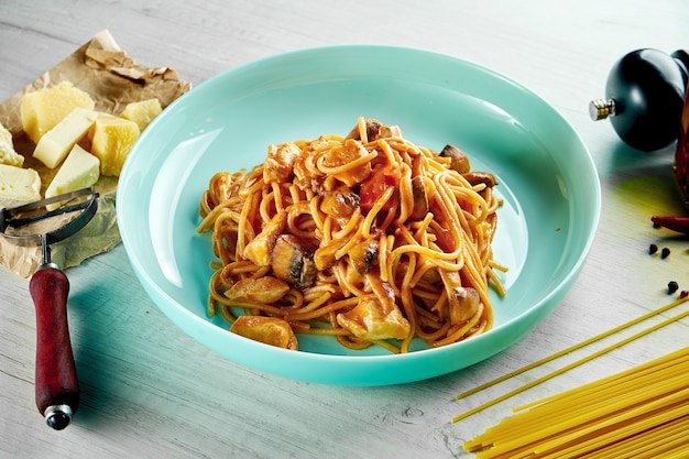 Italienische Spaghetti-Nudeln mit roter Sauce, Hühnchen, Pilzen und Parmesan, serviert in einem blauen Teller auf einem Holztisch. Restaurant Essen.