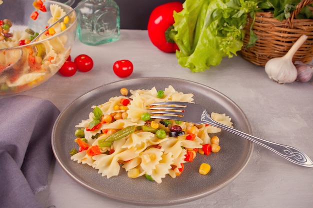 Italienische Teigwaren Farfalle mit Mischungsgemüse auf einer grauen Platte auf einem grauen Hintergrund.