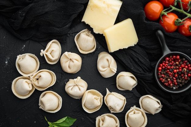 Italienische Tortellini mit frischen Ricotta-Blättern und Tomaten auf schwarzem Tisch, Draufsicht flach gelegt