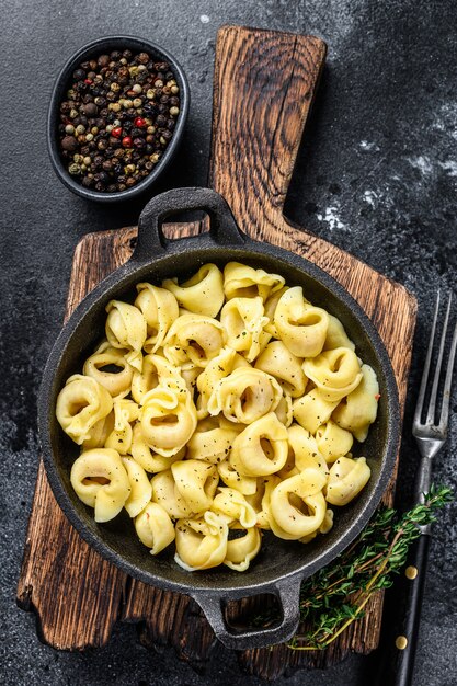 Italienische Tortellini-Nudeln mit Käsesauce in einer Pfanne. Schwarzer Hintergrund. Ansicht von oben.