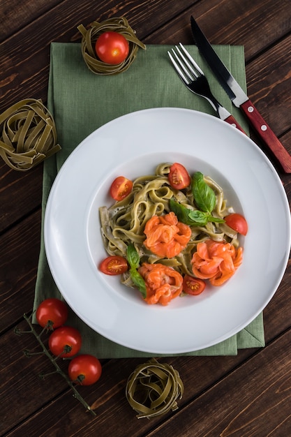 Italienische traditinal Teigwaren der Bandnudeln mit Forelle nah oben auf einer weißen Platte. Tischbesteck und Tomaten auf dem hölzernen Hintergrund