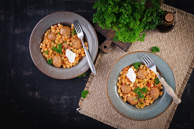 Italienische traditionelle Ditalini-Nudeln mit Fleischbällchen in Tomatensauce und Gemüse in einer Schüssel. Ditalini-Nudeln und Rindfleischbällchen mit Marinara-Tomatensauce. Ansicht von oben. Flach liegen.