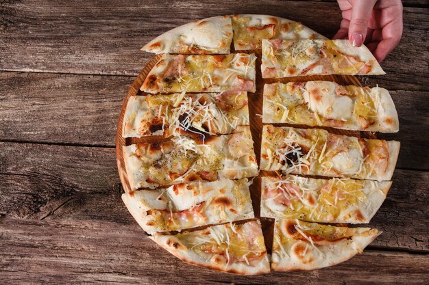 Italienische traditionelle Küche. Hand, die ein Stück appetitanregende frische leckere Pizza auf rustikalem Holztisch serviert.