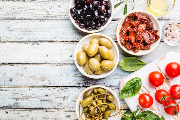 Italienische Vorspeise von oben. Mediterranes Snack-Sortiment. Draufsicht auf schwarze Oliven, Kapern, Olivenöl und sonnengetrocknete Tomaten.