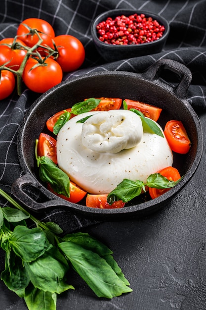 Italienischer Büffel-Burrata-Käse mit Basilikumblättern und Tomaten. Capresesalat. Schwarzer Hintergrund. Draufsicht