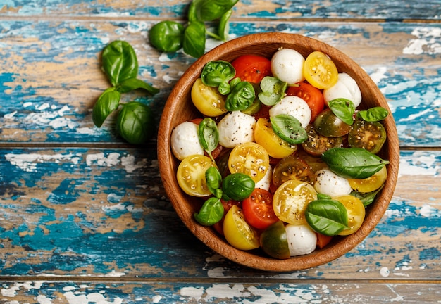 Italienischer Caprese-Salat mit geschnittenen Tomaten, Mozzarella, Basilikum, Olivenöl in Holzschale.