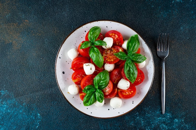 Italienischer Caprese-Salat mit in Scheiben geschnittenen Tomaten Mozzarella Basilikum Olivenöl auf dunklem Hintergrund Draufsicht Italienisches Essen Gesunder Salat Sommerkost