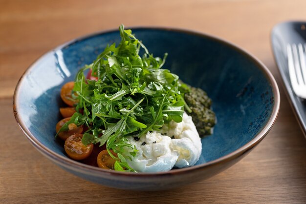 Italienischer Frischkäse Burrata mit buntem Kirschtomatensalat, Rucola und Basilikum mit Pesto-Sauce auf dem Tisch