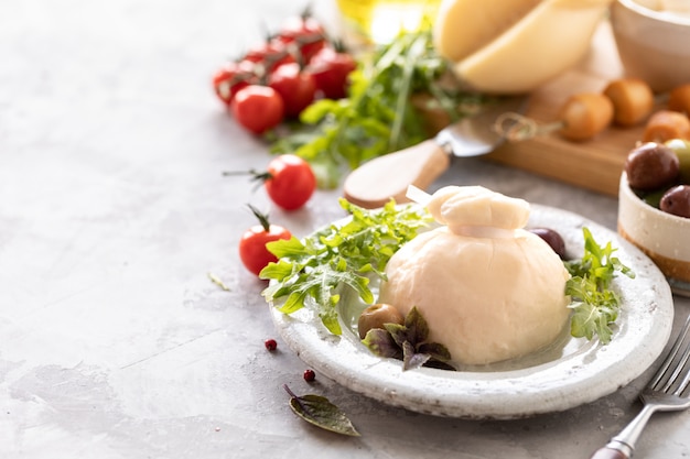 Italienischer Käse Burrata, Mozzarella, Scorocia, Boccini mit Oliven, Kirschtomaten und Rucola auf einem runden weißen Teller auf hellem Hintergrund. Speicherplatz kopieren.