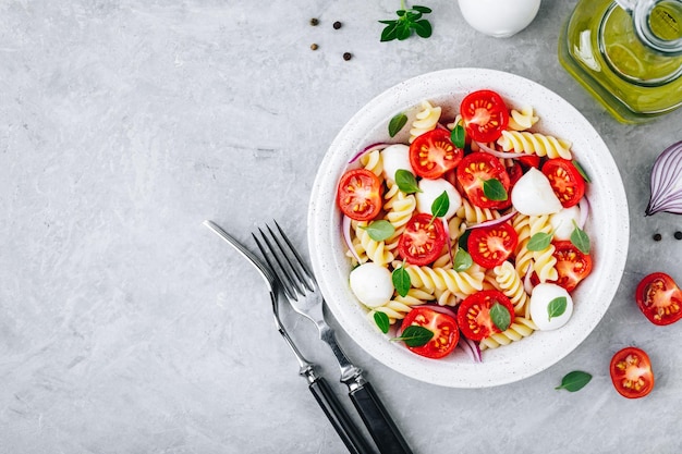 Italienischer Nudelsalat mit Tomaten, Mozzarella-Käse, roten Zwiebeln und Basilikum