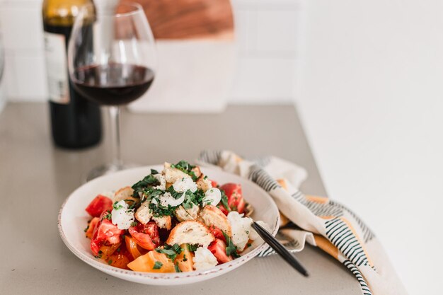 Italienischer Pancanella-Salat auf tiefem Teller, frische Tomaten, Rotwein in einem Glas