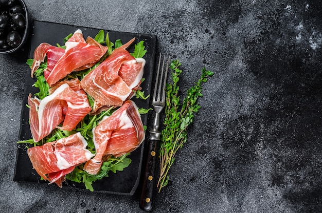 Italienischer Parma-Schinken-Crudo-getrockneter Schinken auf einem Marmorbrett. Schwarzer Tisch. Draufsicht. Speicherplatz kopieren.