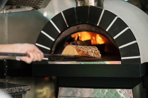 Italienischer Pizza-Holzofen Der Koch füllt den Ofen mit Brennholz