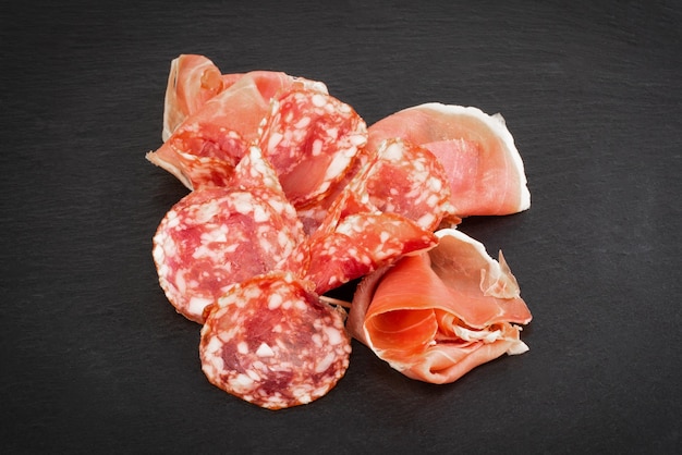 Italienischer Prosciutto Crudo oder spanischer Jamon und Würstchen. Roher Schinken auf Steinschneidebrett.