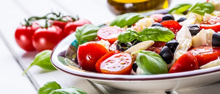 Italienischer Salat Caprese aus Tomaten Mozzarella Käse Oliven Basilikum und Olivenöl.