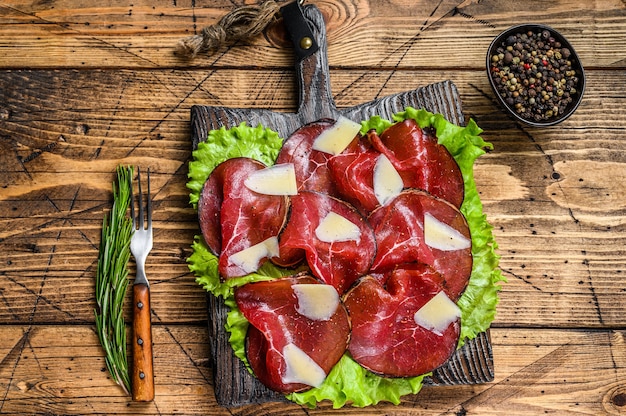 Italienisches Antipasti Bresaola Fleisch geschnitten mit grünem Salat und Parmesan. hölzerner Hintergrund. Draufsicht.