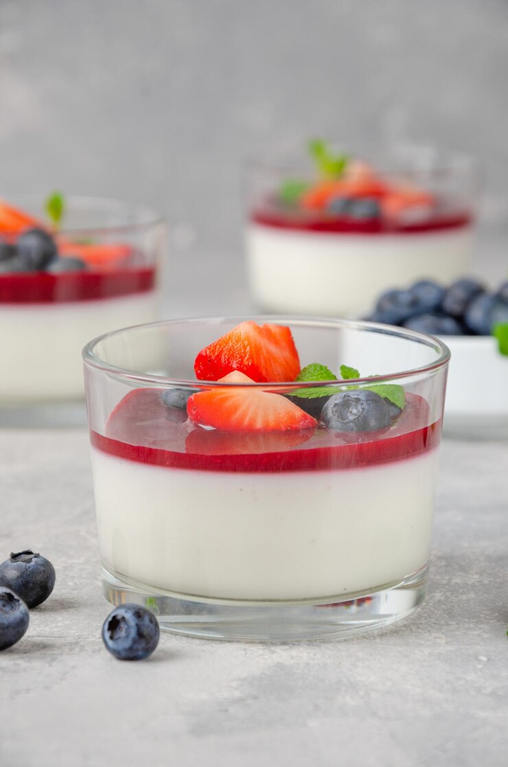 Italienisches Dessert Panna Cotta im Glas mit Beerensauce frische Erdbeeren und Blaubeeren obendrauf
