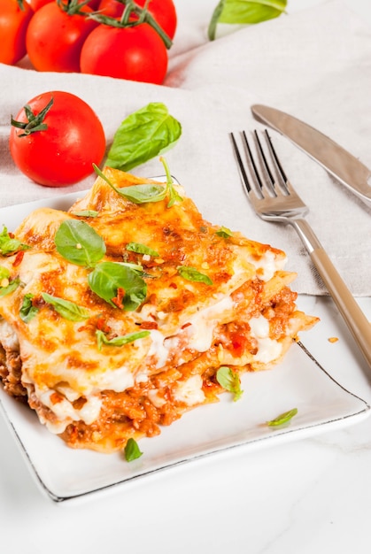 Italienisches Essen Rezept. Abendessen mit klassischer Lasagne Bolognese mit Bechamelsoße, Parmesankäseparmesankäse, Basilikum und Tomaten, auf weißer Marmortabelle, Kopierraum