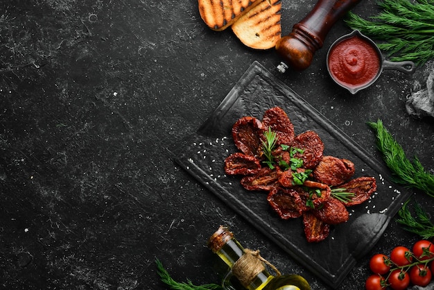 Italienisches Essen Sonnengetrocknete Tomaten mit frischen Kräutern und Gewürzen auf einer schwarzen Steinplatte Draufsicht