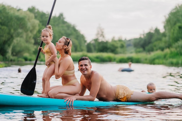 Italienisches Familiensegeln auf Paddelbrett auf dem Fluss, das Spaß hat Kleines Mädchen, das auf Surfbrett mit m steht