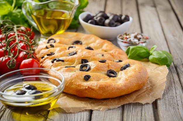 Italienisches Focaccia-Brot mit Oliven und Rosmarin auf rustikalem Holztisch.