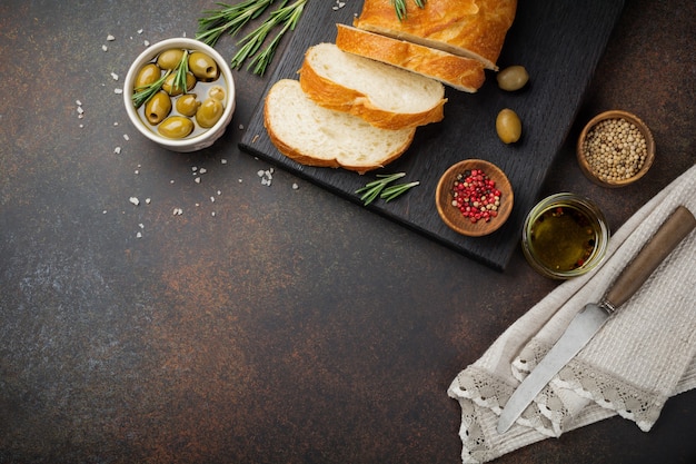 Italienisches traditionelles Ciabatta-Brot mit Oliven, Olivenöl, Pfeffer und Rosmarin auf einer dunklen Betonoberfläche