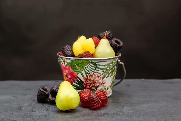 Jabón hecho a mano en forma de bayas y frutas en un cubo de metal sobre fondo negro