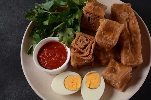 Jachnun oder Jahnun, jemenitisches jüdisches Gebäck, serviert mit frisch geriebenen Tomaten und gekochtem Ei und Zhug, das von den Adeni-Juden stammt und traditionell am Schabbatmorgen in Israel serviert wird.