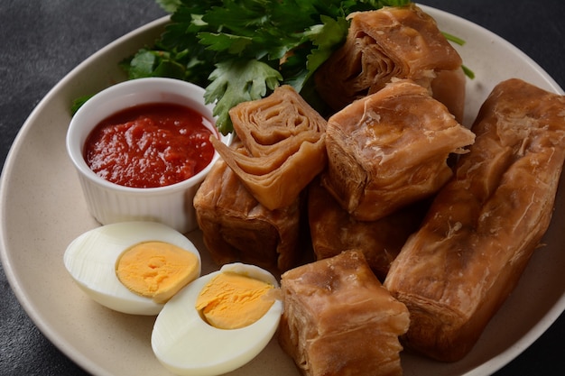 Jachnun oder Jahnun, jemenitisches jüdisches Gebäck, serviert mit frisch geriebenen Tomaten und gekochtem Ei und Zhug, das von den Adeni-Juden stammt und traditionell am Schabbatmorgen in Israel serviert wird.