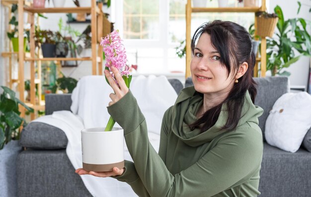 El jacinto de flores de primavera floreció en casa en una maceta en manos de una mujer en el interior de una casa verde con colecciones de estanterías de plantas domésticas Producción de cultivos domésticos