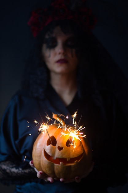 Foto jack-o-lantern. halloween - chica en traje con un patrón en la cara y linterna de calabaza con ojos