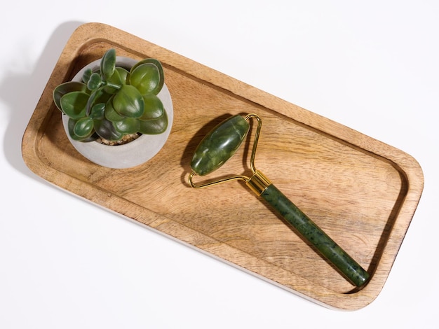 Jade-Gesichtsmassagegerät ein Gegenstand für kosmetische Eingriffe auf einer braunen Holzplatte von oben