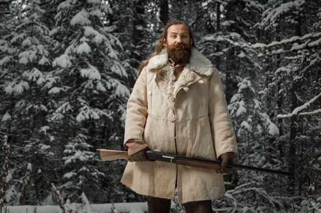 Jäger im Winter Vintage Kleidung mit Bart im Wald mit Pistole