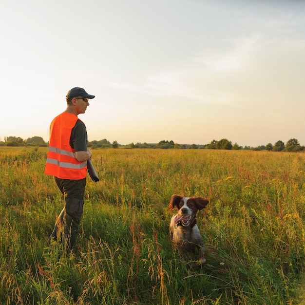 Jäger in der Herbstjagdsaison mit seinem Jagdhund auf Sonnenuntergang.