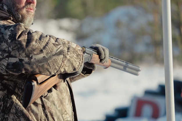 Jäger in Tarnung mit Gewehr im Winterwald. Jagd-Konzept. Mann, der an einem verschneiten Tag eine Reserve sichert. Jäger zielt mit einer Waffe im verschneiten Wald