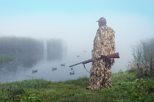 Jäger mit einer Schrotflinte spürt Enten auf dem See auf. Entenjagd.