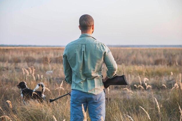 Jäger mit Gewehr und Hund steht auf dem Feld