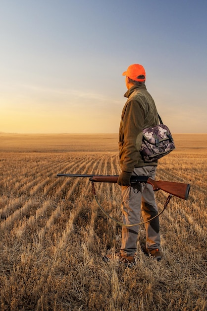 Jäger mit Gewehr zu Fuß im Feld bei Sonnenuntergang Jagdsaison im Herbst Vertikales Bild