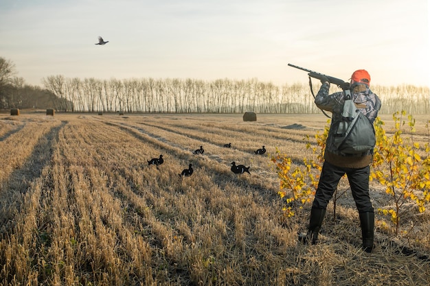 Jäger schießt auf den fliegenden Vogel Jäger in Tarnung mit einer Waffe, die in der Herbstsaison auf Birkhuhn jagt