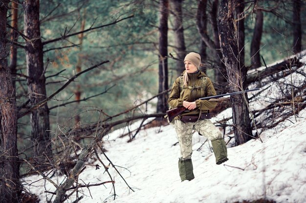 Jägerin in Tarnkleidung, die bereit ist, mit der Waffe zu jagen und im Wald spazieren zu gehen