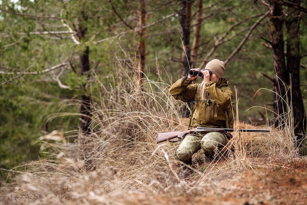 Jägerin in Tarnkleidung, die bereit ist, mit der Waffe zu jagen und im Wald spazieren zu gehen