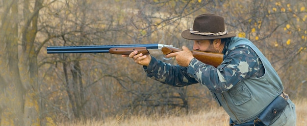 Jägermann in Tarnung mit einer Waffe während der Jagd auf der Suche nach Wildvögeln oder Wild Jagdsaison im Herbst