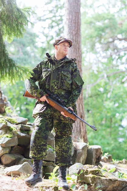 Jagd-, Kriegs-, Armee- und Menschenkonzept - junger Soldat, Ranger oder Jäger mit Waffe im Wald